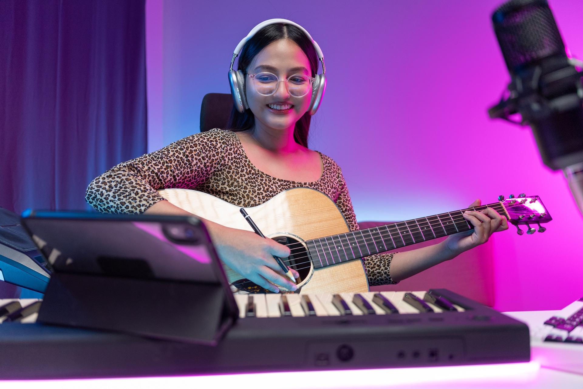 Professional Women Musician composing a song with acoustic guitar, piano keyboard and condenser microphone. She mixing and mastering her song with table at digital recording home studio.